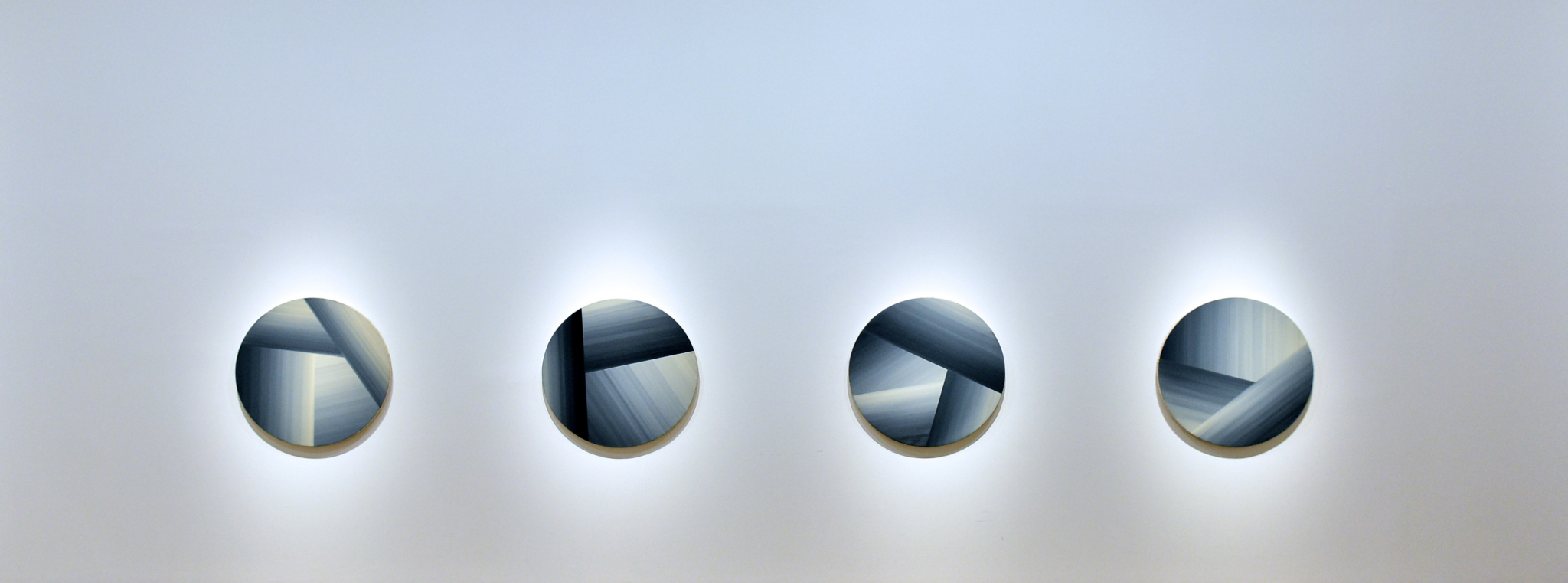 5eb28adc015c0 Trzy okrągłe obrazy na białej ścianie; każdy podzielony na kilka części, odcinających się od siebie za sprawą cieniowania – od bieli do ciemnego granatu; sprawiają wrażenie nawiniętych motków włóczki.