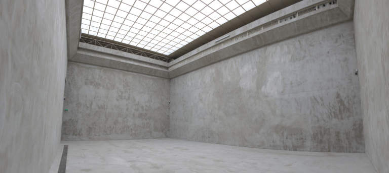 Zdjęcie: puste wnętrze dużej sali, którą przykrywa w całości szklany świetlik, podzielony na kwadratowe segmenty metalowymi listwami; podłogę oraz ściany wraz z gzymsem pomalowano w sposób imitujący strukturę szarego betonu.