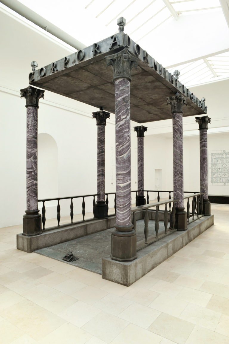 Zdjęcie: białe wnętrze; pośrodku architektoniczny, kamienny baldachim o uproszczonej konstrukcji dachu - w formie płyty, która wydaje się unosić nad 6 kolumnami; kolumny otoczone prostą balustradą.