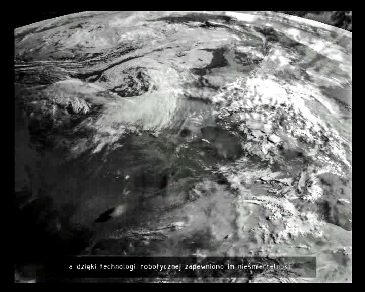 Kadr z filmu. Fragment Ziemi widzianej z kosmosu. Oceany i kontynenty są niewidoczne, bo ukryte za chmurami. Cały kadr jest szary.