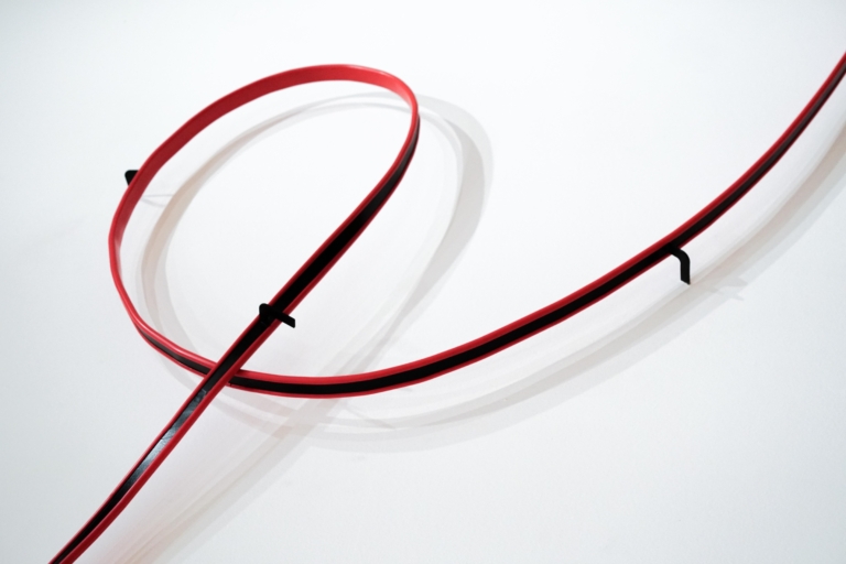 Fragment rzeźby: pętla przymocowana do ściany, z czarnej metalowej poręczy obłożonej czerwonym PCV