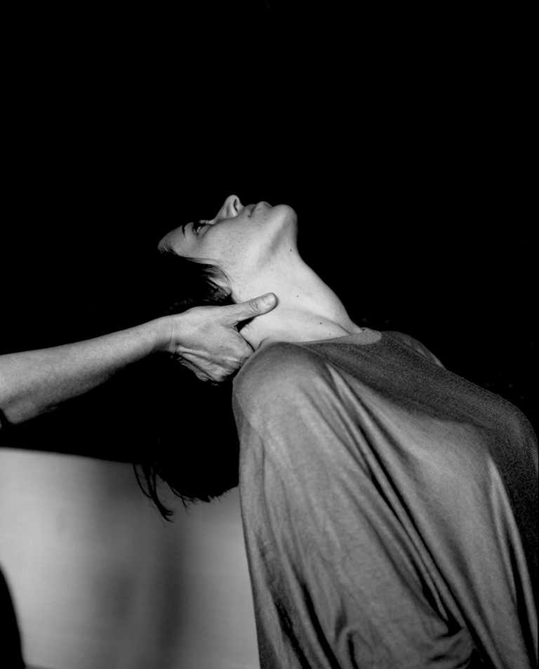 Czarno-białe zdjęcie. Kobieta odchyla głowę do tyłu, druga osoba podtrzymuje jej kark ręką