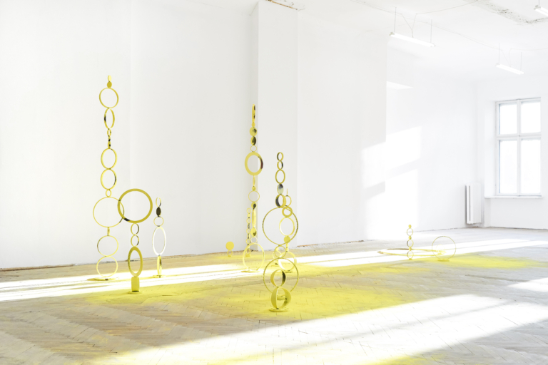 W białej przestrzeni znajduje się 7 abstrakcyjnych rzeźb z metalowych okręgów różnej wielkości. Są proszkowo pomalowane na żółto