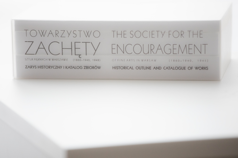 zdjęcie: grzbiet trzy tomowego wydawnictwa o Towarzystwie Zachęty Sztuk Pięknych - biły grzbiet z czarnym liternictwem. Napis po polsku i angielsku: Towarzystwo Zachęty Sztuk Pięknych. Zarys historyczny i katalog zbiorów