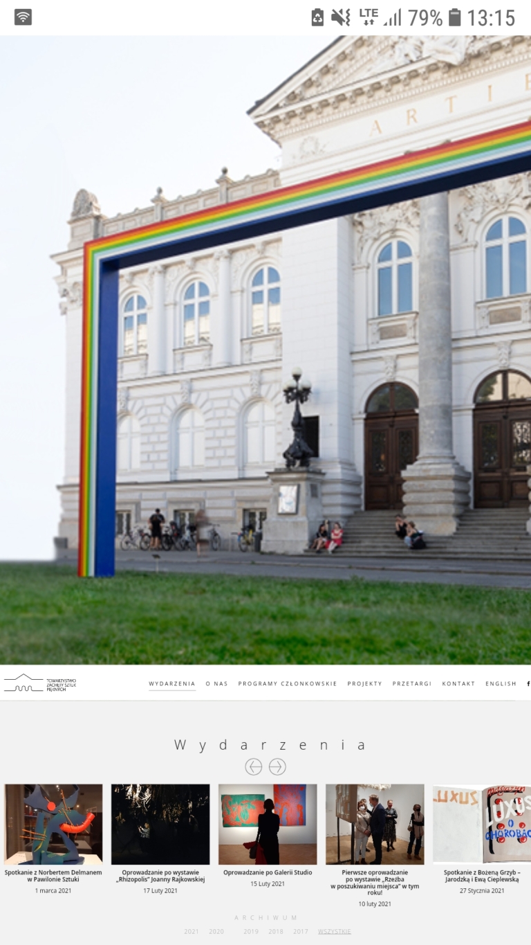 6061b6562f355 Zdjęcie: widok wejścia głównego do Zachęty, przed nim na trawniku stoi prostokątna tęcza z drewna autorstwa Marka Sobczyka