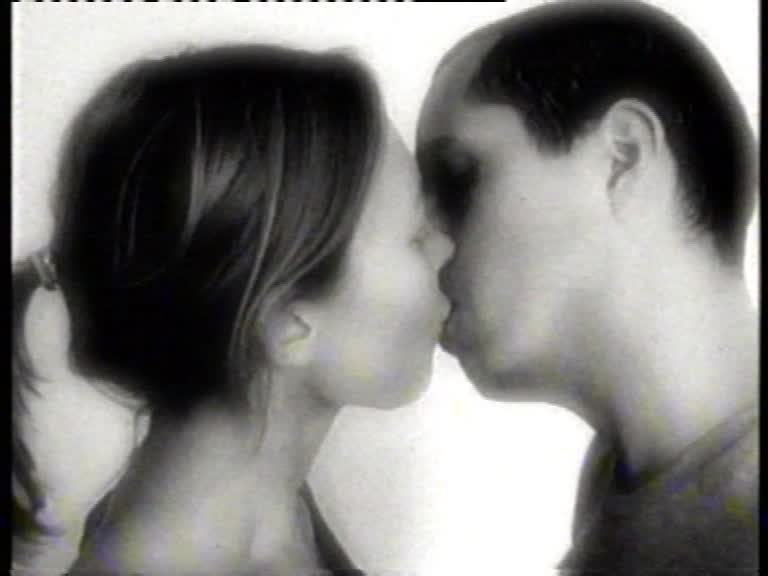 Kadr z czarno-białego filmu. Mężczyzna i kobieta z profilu całują się. Za nimi jasne tło.