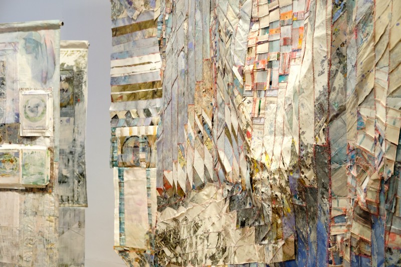 Zbliżenie na jeden z obrazów na wystawie; powierzchnia składa się z małych kawałków płótna zszytych ze sobą; przewaga jasnych kolorów