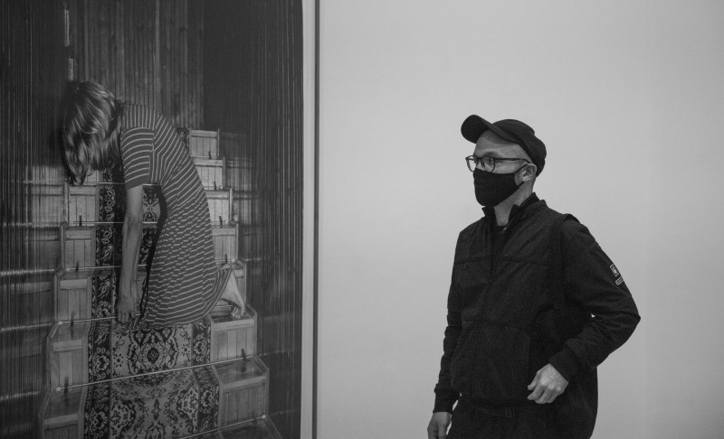 zdjęcie: zdjęcie z wystawy. Młody człowiek w czapce i masce przygląda się fotografii Joanny Piotrowskiej przedstawiającej kobietę klęczącą na schodach