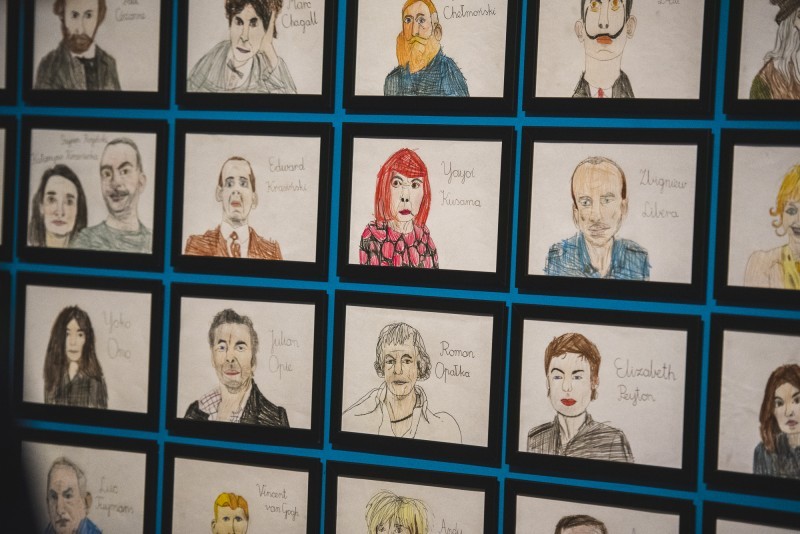 a zdjęciu: ściana sali wystawowej gęsto zawieszona portretami artystek i artystów wykonanych przez kilkunastoletniego Tymona Rogalskiego