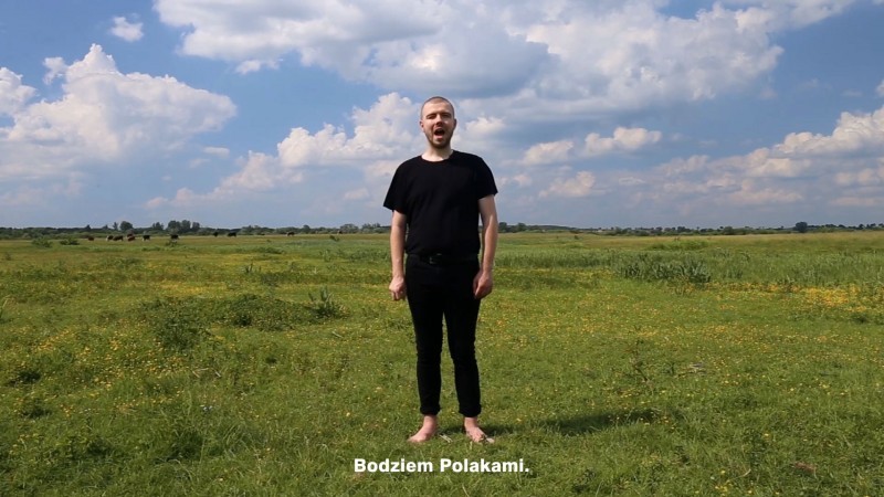 zdjęcie: młody mężczyzna stoi boso na trawie. pod stopami ma napis "Bodziem Polakami"