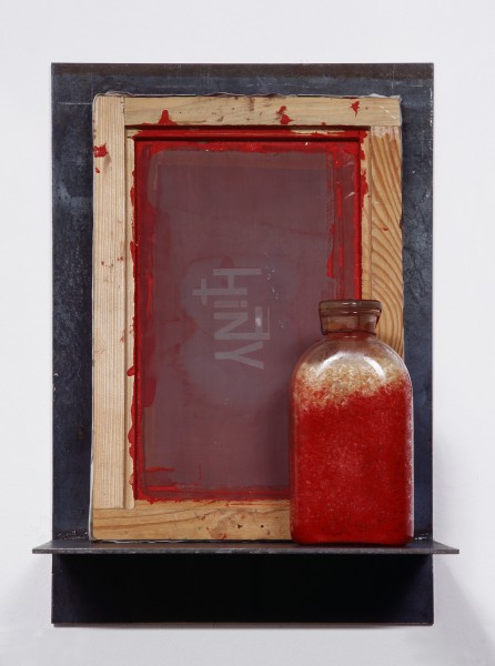 zdjęcie: na odwrociu niewidocznego obrazy namalowany jest napis HINY. Obraz, wraz ze szklaną butelką napełnioną ryżem zabarwionym na czerwono, stoi na wąskiej metalowej półce