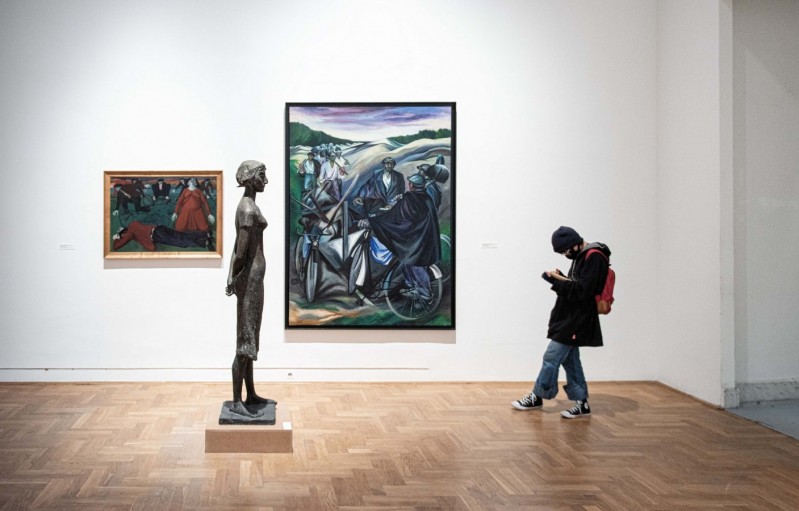 Zdjęcie: sala wystawowa, na ścianie dwa obrazy - większy i mniejszy, pomiędzy nimi rzeźba ludzkiej postaci ustawiona profilem, naprzeciw rzeźby stoi dziecko z czerwonym plecakiem.