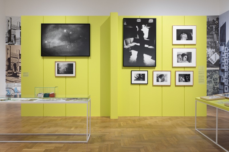 Zdjęcie: widok wystawy. Na środku ściana w kolorze jaskrawozielonym. Na niej prezentowane są czarno-białe fotografie w różnych formatach.
