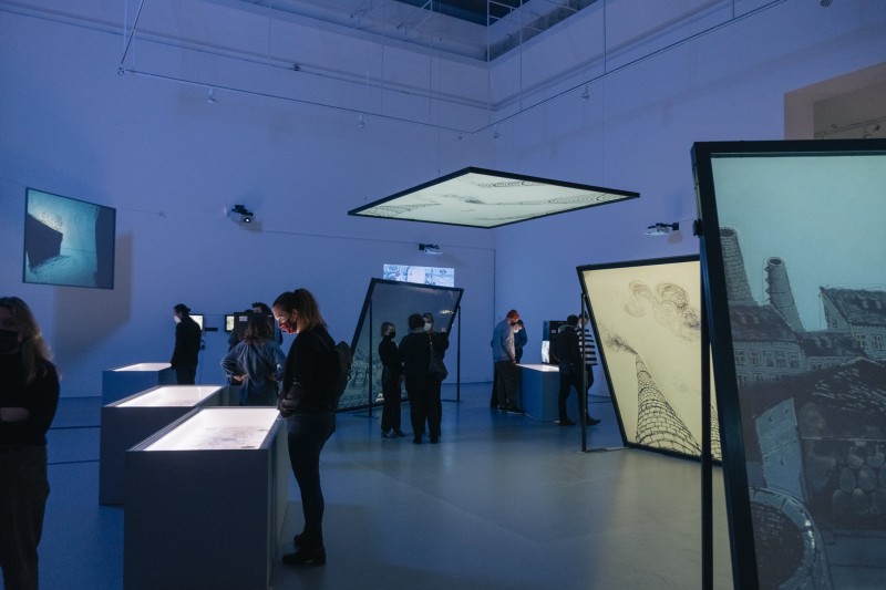 Ludzie w przestrzeni wystawy Wilczynskiego otoczeni świecącymi ekranami.