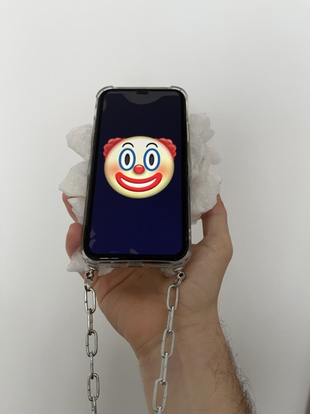 Dłoń trzymająca telefon komórkowy. Na ekranie emotikonka clowna