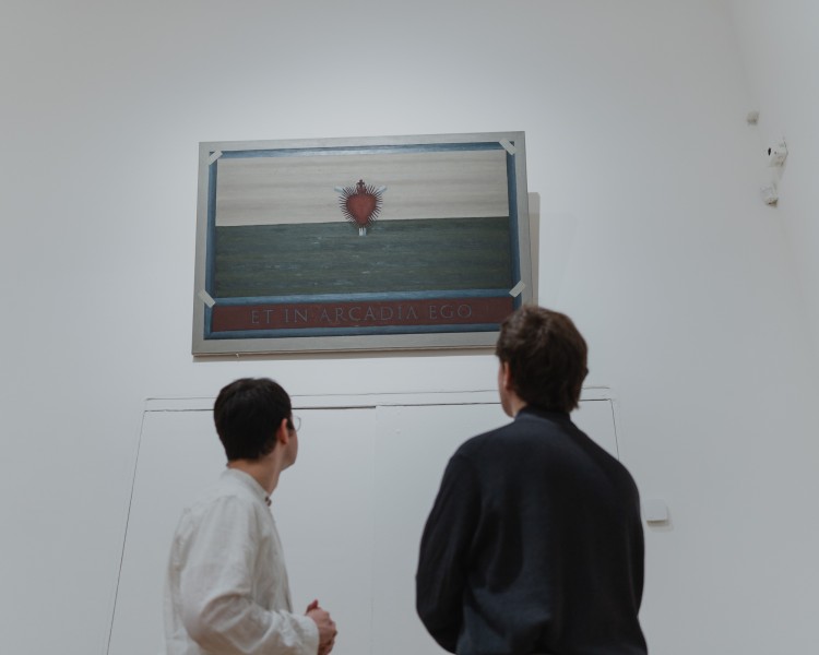 Dwie osoby stojące w przestrzeni wystawy. Wpatrują się w górę oglądając obraz przedstawiający płonące serce.