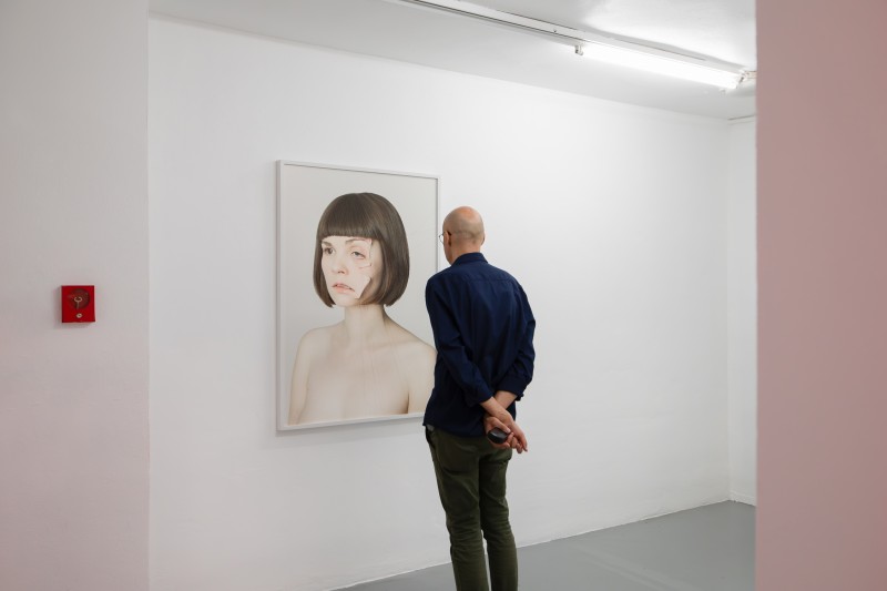 Człowiek stojący tyłem spogląda na niepokojącą fotografię kobiety wiszącą na białej ścianie