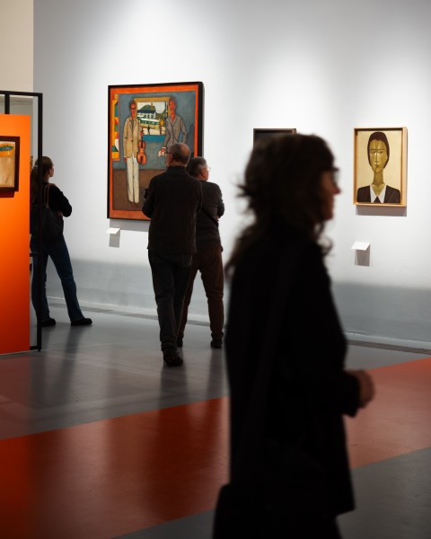 Zdjęcie; kadr przedstawiający kilka prac oraz zwiedzających ekspozycję Jerzy Nowosielski.