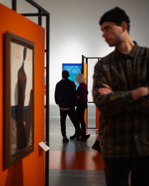 ALT: Zdjęcie; kadr przedstawiający osoby zwiedzające oraz kilka prac z wystawy Jerzy Nowosielski.