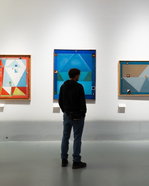 Widok wystawy, postać na tle niebieskiego obrazu zawieszonego na ścianie.