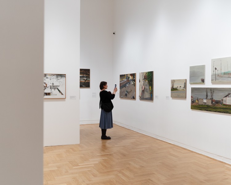 Zdjęcie; kadr przedstawiający kilka prac z wystawy oraz osobę zwiedzającą wystawę Krzysztof Klimek. Teraz wolę widoki