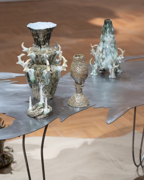 ALT: zdjęcie; na metalowym stoliku o nieregularnym kształcie blatu ustawione cztery ceramiczne naczynia z kolczastymi elementami.