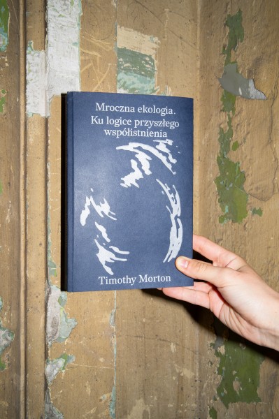 zdjęcie, dłoń trzymająca granatową książkę na tle ściany ze schodzącą farbą