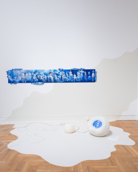 Widok wystawy, na białej ścianie błękitny pas, zdjęcie. Biała rozlana plama na drewnianej podłodze poniżej