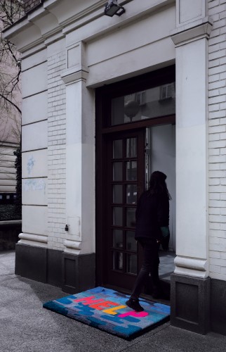 Wejście do budynku, osoba ubrana na czarno przechodzi przez kolorową wycieraczkę z napisem "help".