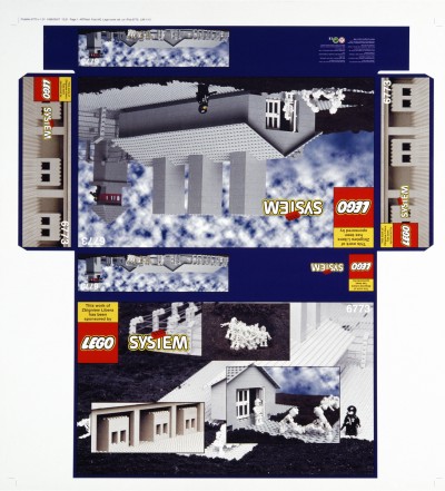 Na płasko rozłożone pudełko od klocków LEGO – na nim widnieje zdjęcie baraku z obozu koncentracyjnego zbudowanego z szarych klocków. Przed barakiem widać ludziki LEGO – strażnik i zmarli więźniowie.
