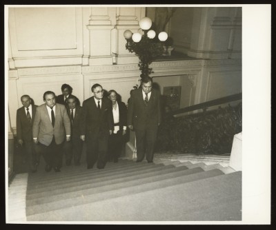 Czarno-białe zdjęcie. Sześciu mężczyzn w tym reprezentanci Japonii i jedna kobieta. Wchodzą po schodach Zachęty. Z prawej strony kuta, ozdobna balustrada i kandelabr. 