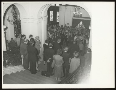 Czarno-białe zdjęcie. W holu Zachęty tłum ludzi. Kilkanaście osób stoi na schodach, reszta, czyli większość stoi poniżej w przestrzeni holu głównego.