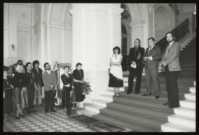 Czarno-białe zdjęcie. Hol główny Zachęty. Na schodach cztery osoby, poniżej po lewej grupa osób w tym dwie kobiety z bukietami ciętych kwiatów.