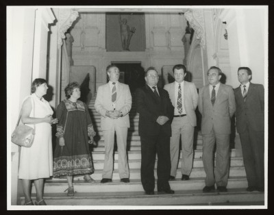 Czarno-białe zdjęcie. Dwie kobiety i pięciu mężczyzn, stoją na wewnętrznych schodach Zachęty. W tle zdobiona klatka schodowa i rzeźba we wnęce.
