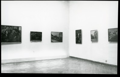 Czarno-białe zdjęcie. Narożnik sali wystawowej. Na ścianach pięć realistycznych obrazów.