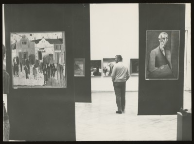 Czarno-białe zdjęcie. Przestrzeń Wystawy. Dwie kobiety i mężczyzna oglądają zawieszone na ścianach wokół nich obrazy.