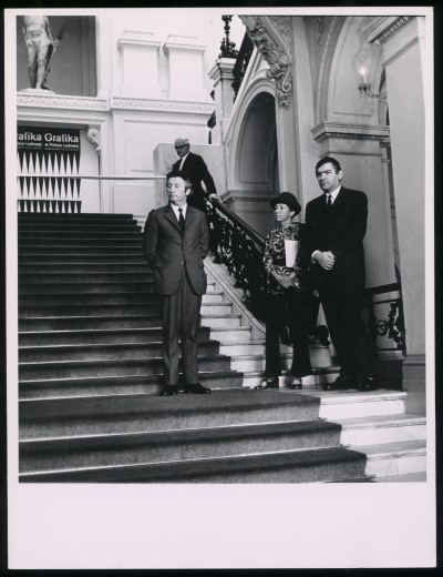 Czarno-białe zdjęcie. Wnętrze Zachęty. Na schodach stoi dwóch mężczyzn, a między nimi niewysoka kobieta. Dalej i wyżej kolejny mężczyzna.