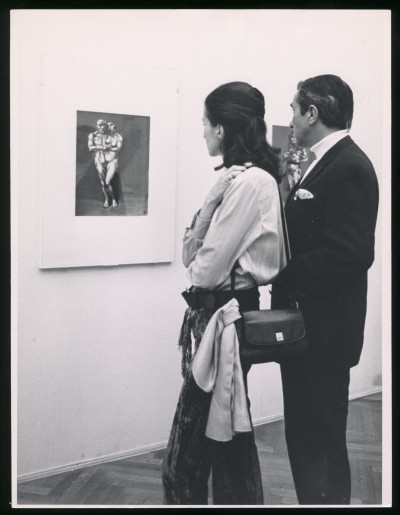 Czarno-białe zdjęcie. Grupa zwiedzających ogląda wiszące na ścianach grafiki.