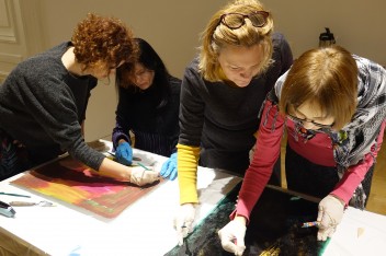 Na zdjęciu cztery pracujące w parach uczestniczki szkolenia skupione nad zamalowanymi farbą kartkami papieru.