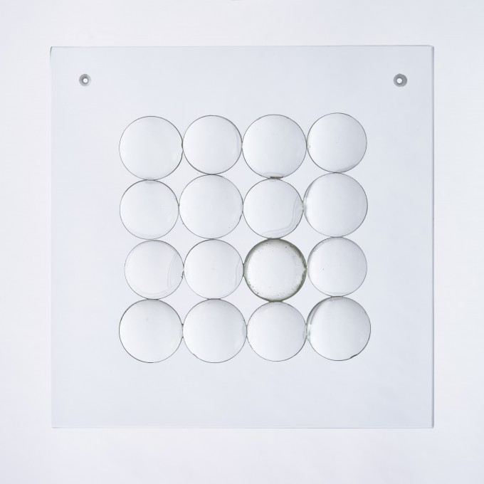 Szklana kompozycja przestrzenna w formacie kwadratu. Na przezroczystej szklanej tafli okrągłe soczewki ułożone jedna przy drugiej w czterech rzędach i czterech kolumnach.