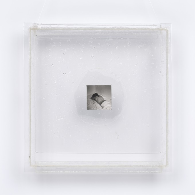 Instalacja z przezroczystej pleksi o formacie kwadratu. Na środku kwadratu zaznaczony okrąg, jak soczewka. W nim, między dwoma płytkami pleksi, dwie małe odbitki czarno-białej fotografii, przedstawiającej nagie plecy osoby leżącej na brzuchu w białej pości