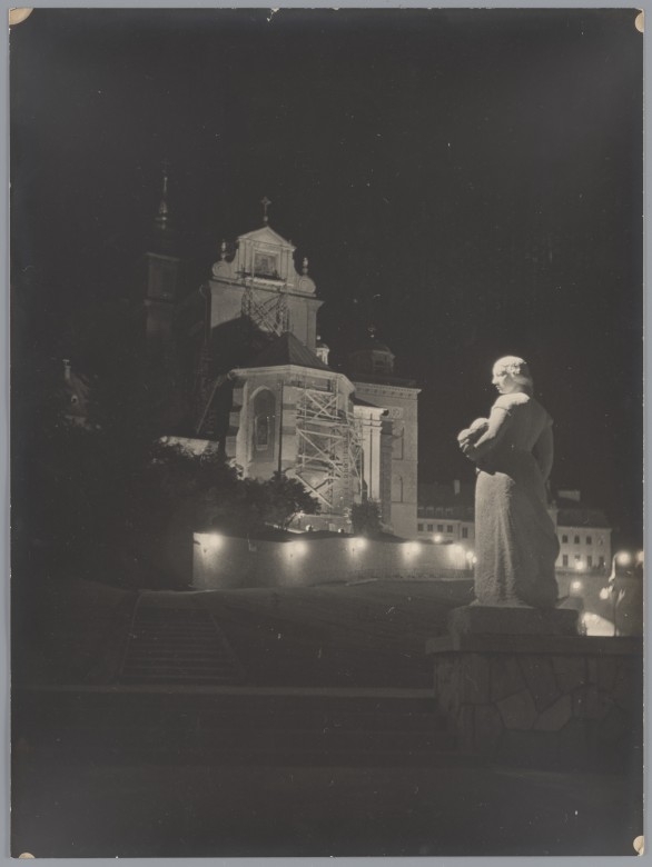 Noc. Na pierwszym planie biała rzeźba przedstawiająca kobietę. W tle oświetlony kościół, wokół którego stoją rusztowania.
