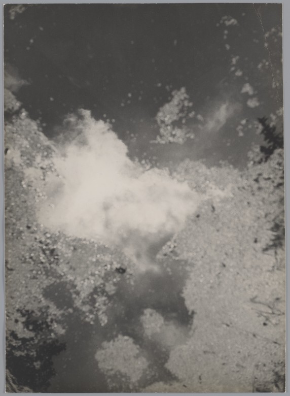 Bardzo nieostre zdjęcie. W kałuży na asfalcie odbity fragment nieba z białymi chmurami.