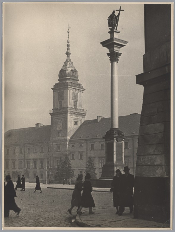 Plac Zamkowy z Kolumną Zygmunta, spacerują po nim ludzie, głównie pary. W tle Zamek Królewski, przed nim kilka choinek.