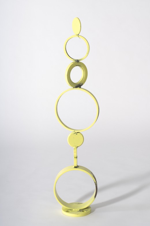 Abstrakcyjna rzeźba z niedokładnie pomalowanej na żółto stali. Tworzy ją kilka różnej wielkości i grubości okręgów i pełnych kół, ustawionych jeden na drugim w rodzaj kolumny lub totemu. Ustawione pod różnymi kątami względem siebie, jak skręcony łańcuszek.