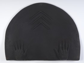 Płaskorzeźba z terakoty, wyglądem przypomina nieco matowy, prawie czarny metal. Płyta w formie półokręgu. Przy prostej dolnej krawędzi szeroko rozstawione realistyczne dłonie. Wyżej wypukły symbol w formie trzech "daszków" jeden nad drugim.