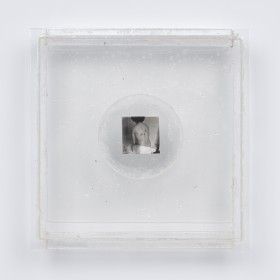 Instalacja z przezroczystej pleksi o formacie kwadratu. Na środku kwadratu zaznaczony okrąg, jak soczewka. W nim, między dwoma płytkami pleksi, dwie małe odbitki czarno-białej fotografii, przedstawiającej nagie plecy siedzącej tyłem osoby. Pomiędzy płytkam