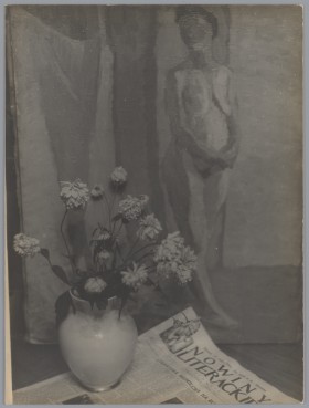 Wazon z kwiatami stojący na gazecie "Nowiny Literackie". W tle płótno z namalowanym na nim aktem kobiecym.