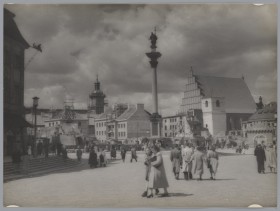 Plac Zamkowy w Warszawie w czasie odbudowy. Przy kamienicach stoją rusztowania. Na środku placu Kolumna Zygmunta, wokół niej spacerują ludzie.