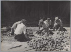 Siedzący na ziemi mężczyźni układają chodnik z kostki brukowej.